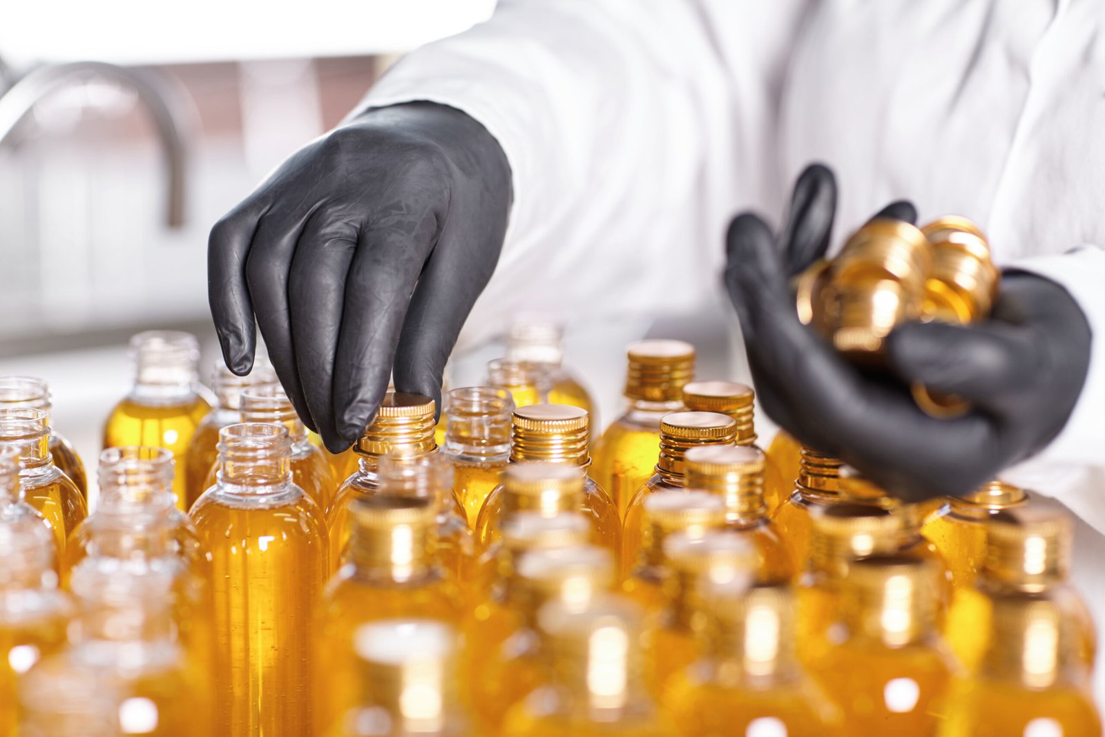 selective focus of factory worker's hands in black gloves closing bottles in front of him with screw caps at laboratory. mass production and manufacturing. medicine, cosmetics and pharmacy concept